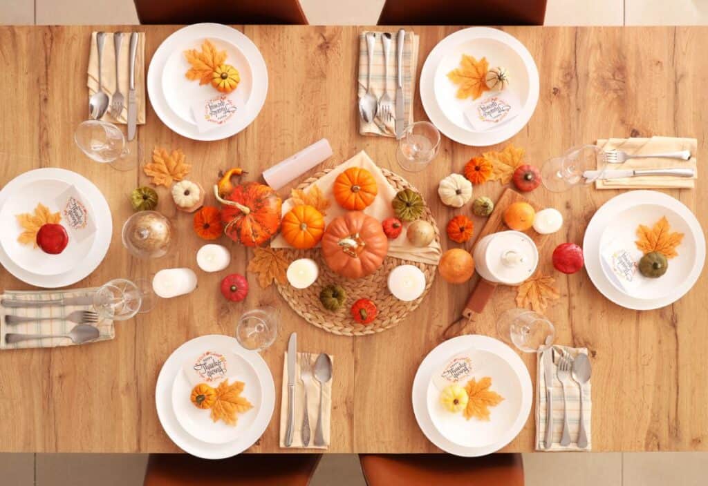 A wooden table set for six with white plates, plaid napkins, cutlery, and autumn-themed decorations including mini pumpkins, leaves, and candles&mdash;ready for a festive meal with no pie in sight.