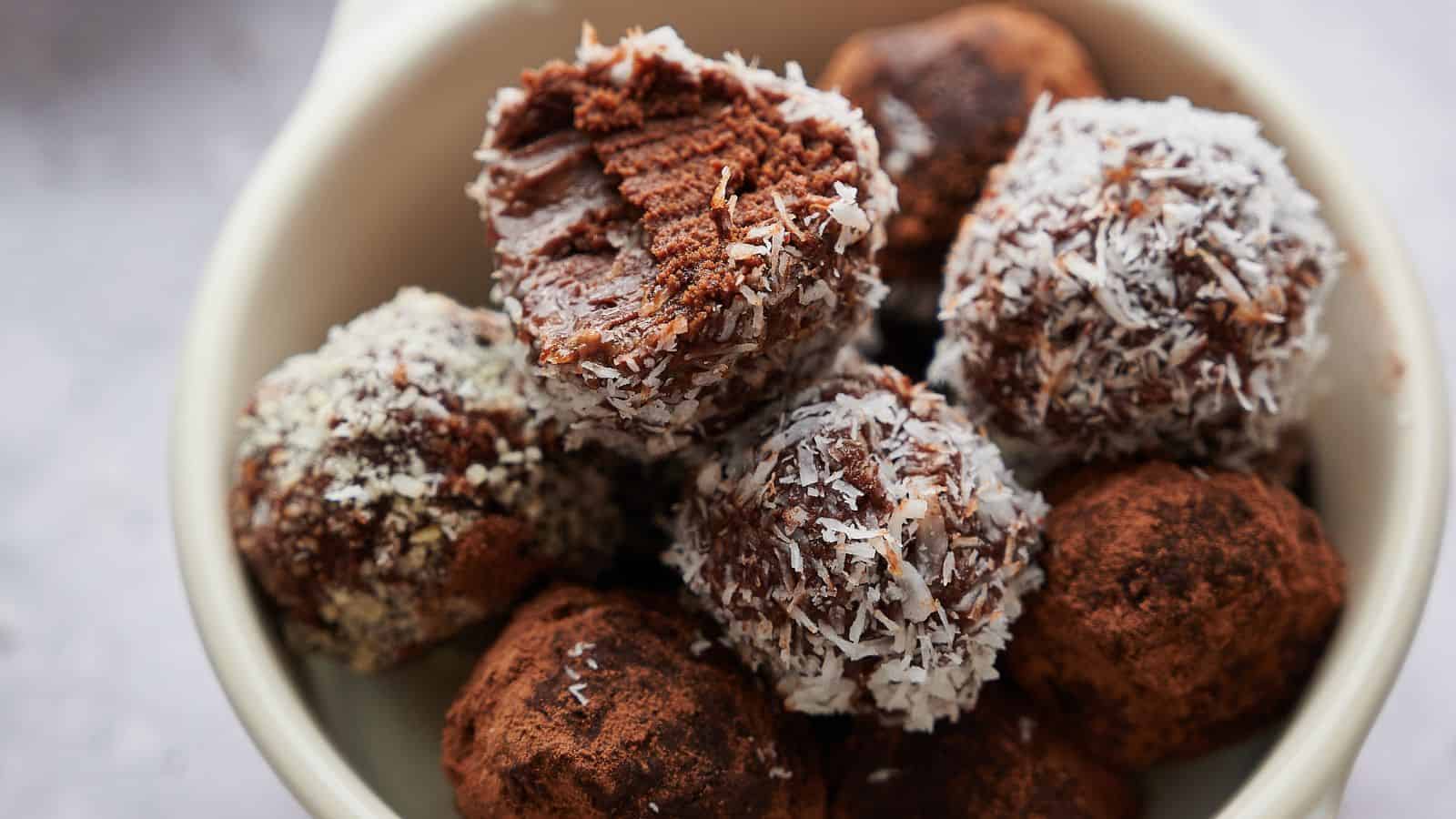A bowl containing chocolate truffles, some coated with shredded coconut and others with cocoa powder; one truffle has a bite taken out of it.