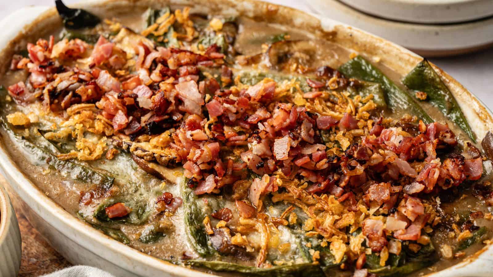 A baked casserole topped with chopped bacon, crispy onions, and melted cheese, featuring visible green peppers and a creamy sauce.
