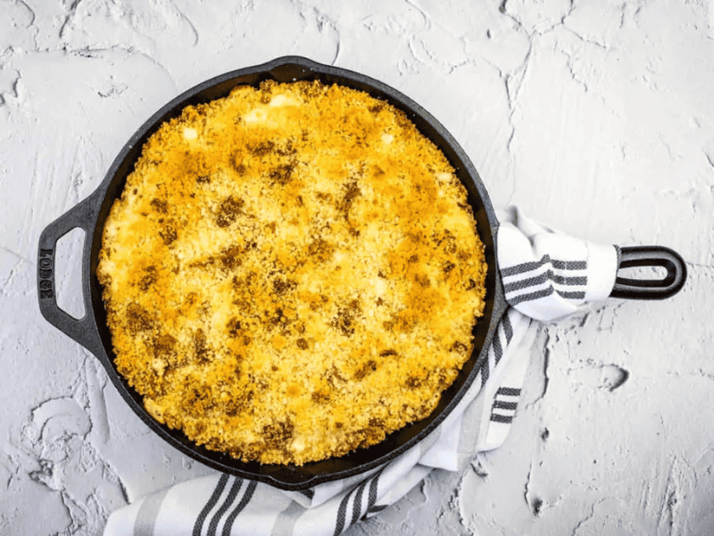 A cast iron skillet filled with baked macaroni and cheese topped with golden breadcrumbs, resting on a textured white surface with a striped kitchen towel.