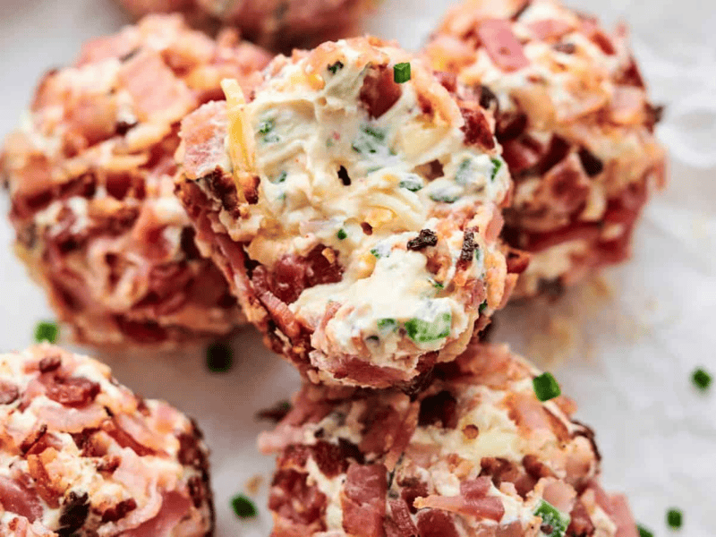 Close-up of several Bacon Jalapeno Popper Cheese Balls wrapped in bacon, stuffed with cheese, and seasoned with herbs and spices, placed on crumpled parchment paper.