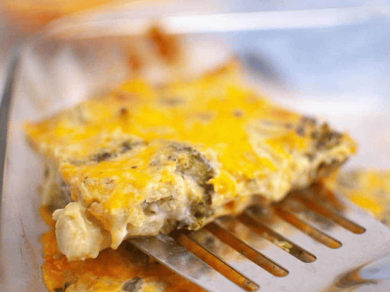 A metal spatula lifts a slice of 3-Ingredient Broccoli Cheese Casserole from a glass baking dish.