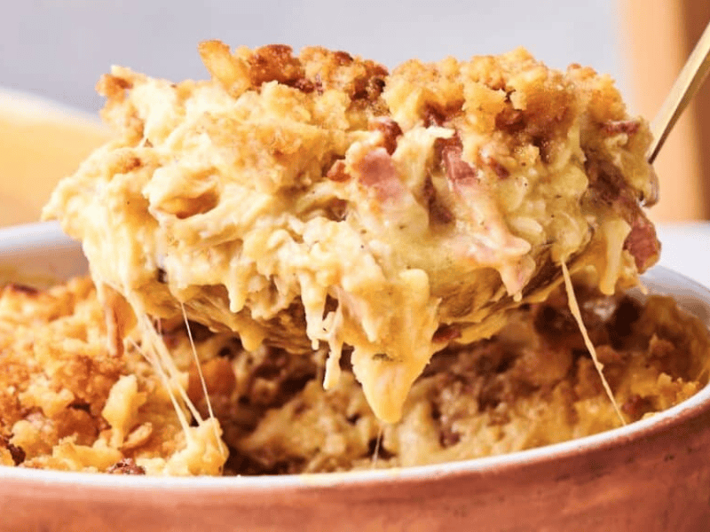 A spoon lifts a serving of baked macaroni and cheese with a golden breadcrumb topping and melted cheese from a casserole dish.