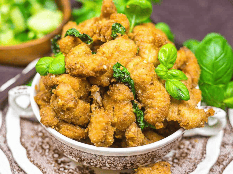 A bowl of crispy fried chicken garnished with basil leaves.