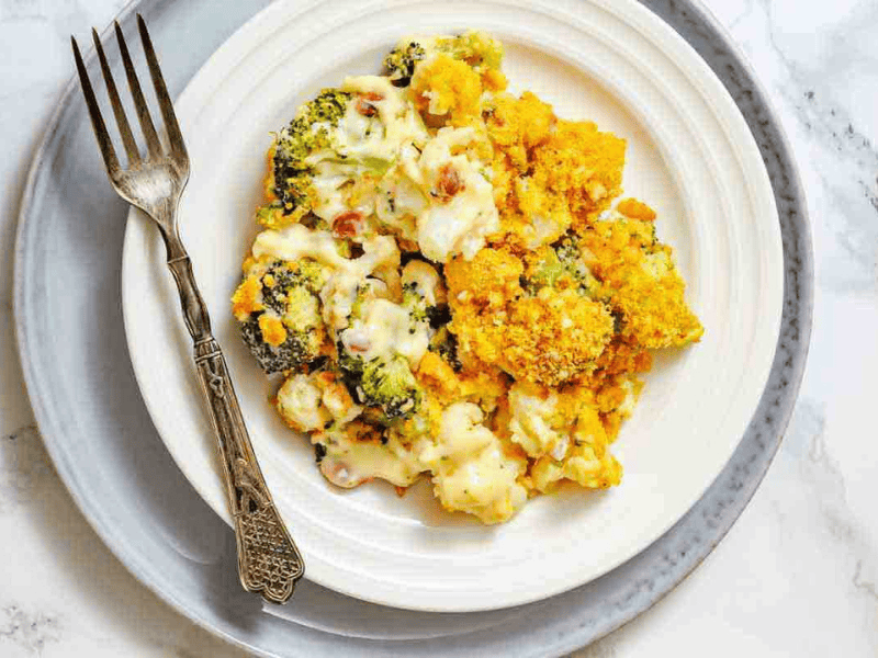 A serving of broccoli and cauliflower casserole with a golden crumb topping on a white plate, accompanied by a fork.