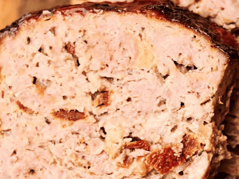 Close-up of a slice of cooked meatloaf showing its texture and bits of embedded vegetables.