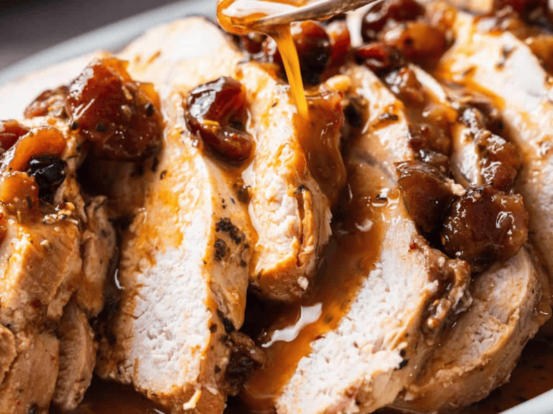 Sliced cooked turkey breast topped with a chunky fruit sauce, with additional sauce being drizzled over the slices.