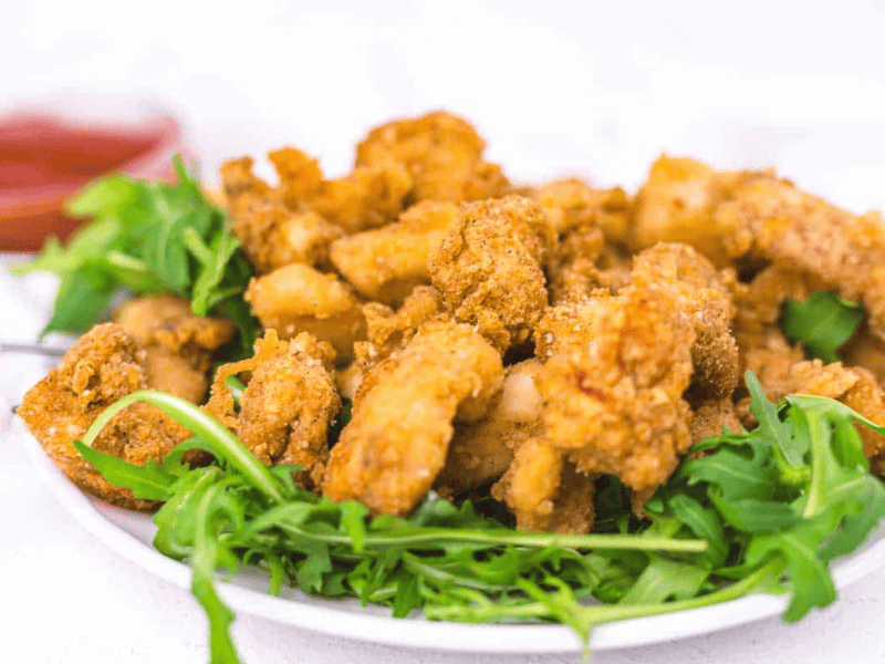 A plate of fried chicken pieces served on a bed of fresh arugula, with a small bowl of dipping sauce in the background.