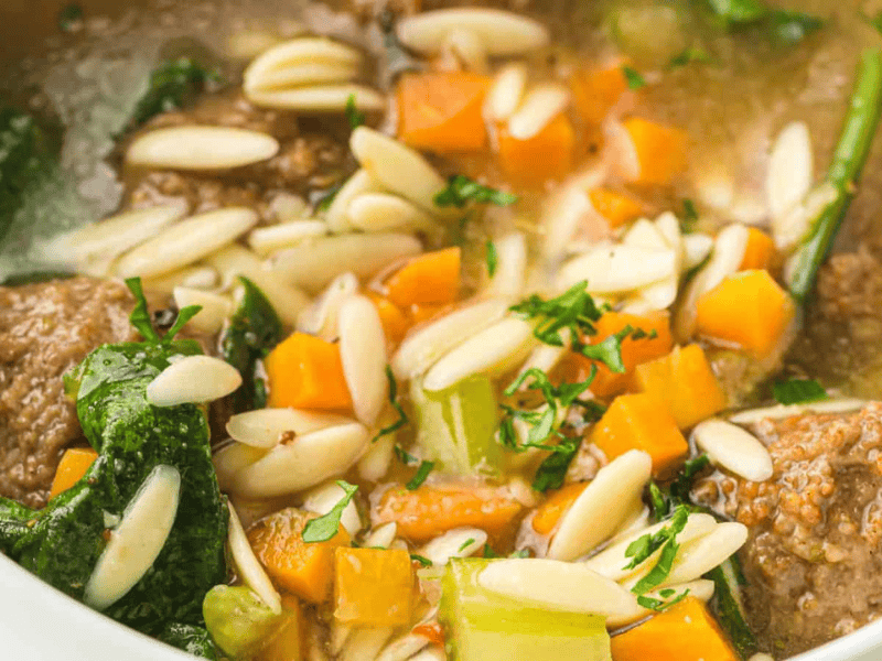 A close-up of a spoon holding a meatball in a bowl of Slow Cooker Italian Wedding Soup.