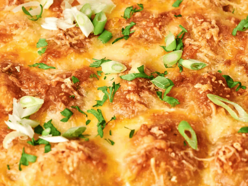 Close-up of a cheesy baked dish topped with chopped green onions and fresh herbs.