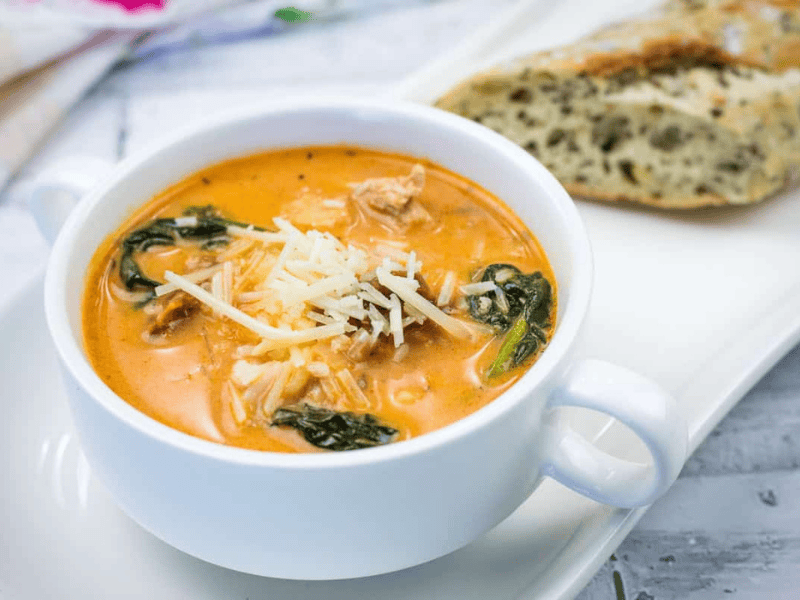 A bowl of Marry Me Chicken Soup accompanied by a piece of bread on a white plate.