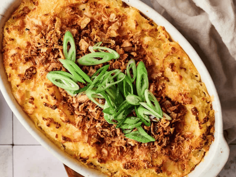 A baked casserole topped with crispy fried onions and sliced green onions, served in a white oval dish.
