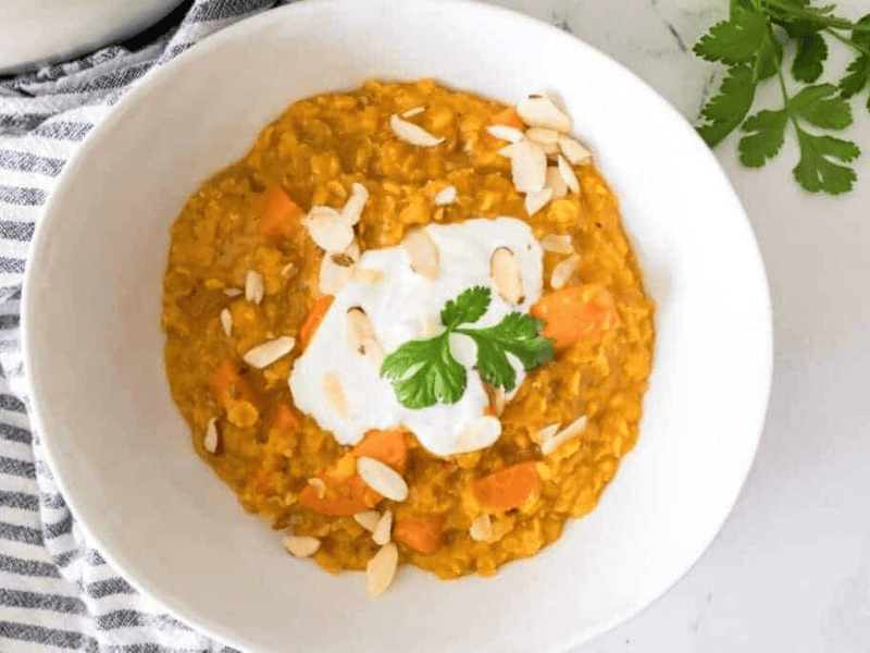 A bowl of carrot and lentil soup topped with yogurt, cilantro, and almond slices.