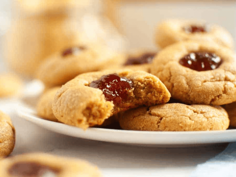 A close-up of peanut butter thumbprint cookies filled with red jelly.
