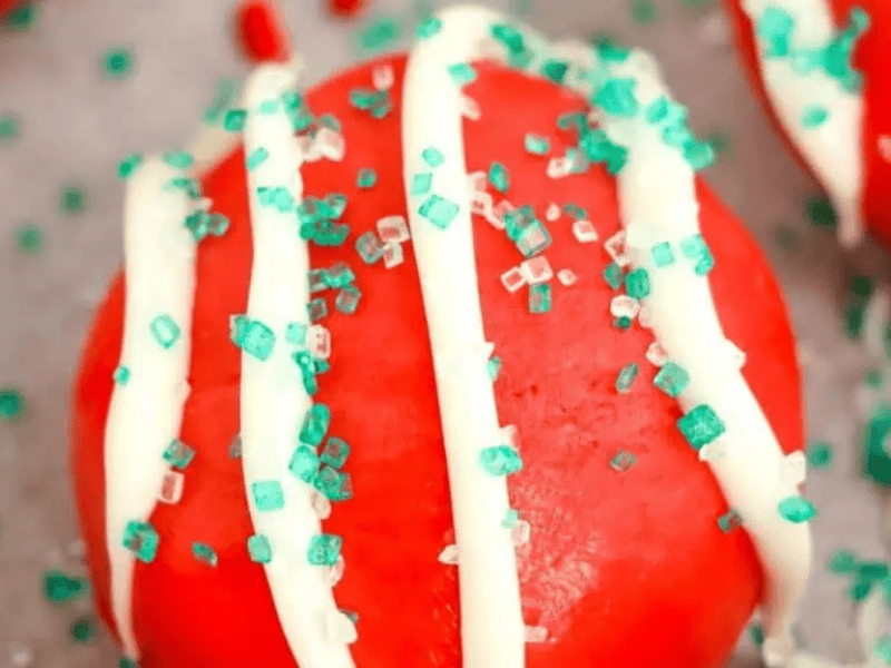 A round red cookie with white icing drizzles and green sugar sprinkles on top.