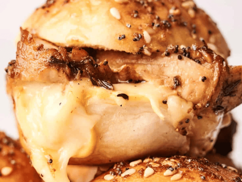 Close-up of a seasoned bagel sandwich with melted cheese and turkey slider filling, topped with seeds.