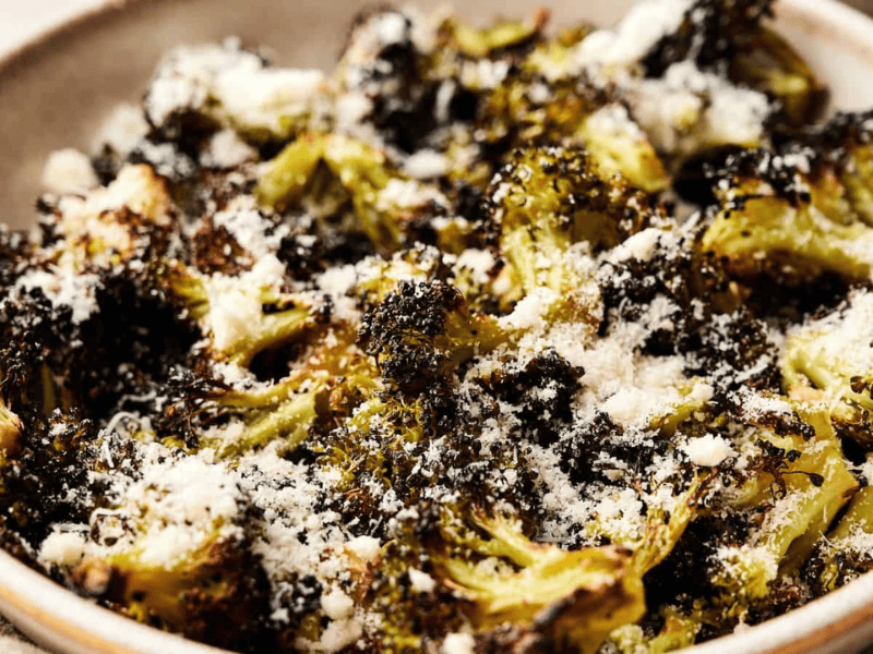A bowl of roasted broccoli florets topped with grated parmesan cheese.