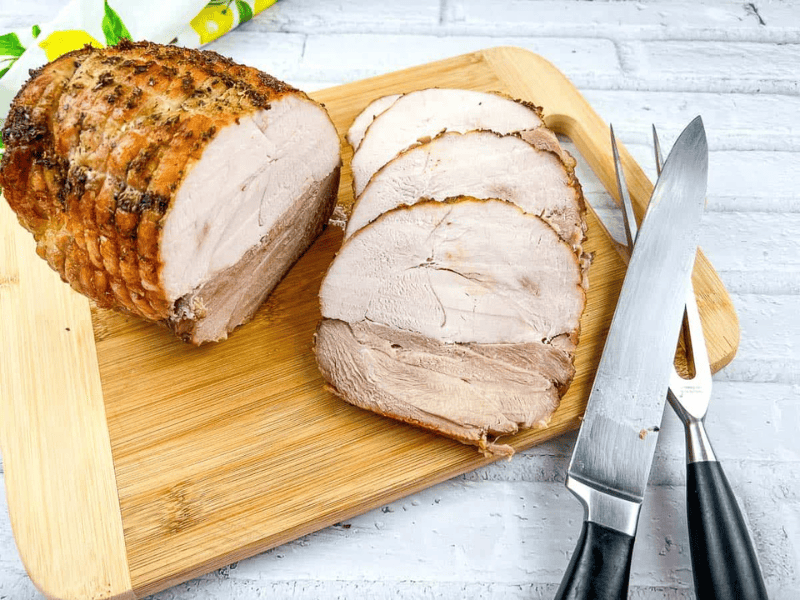 Sliced roasted pork on a wooden cutting board, with a carving knife and fork beside it.