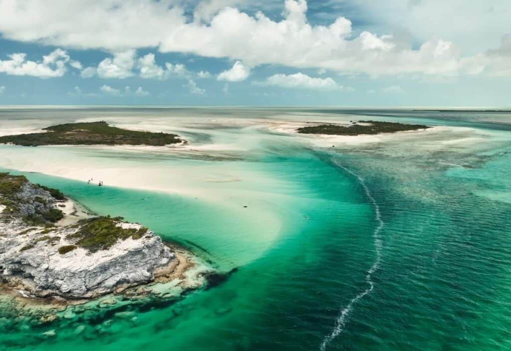 Aerial view of the stunning Turks and Caicos coastline with turquoise water, white sandy beaches, rocky cliffs, and scattered small islands under a partly cloudy sky.