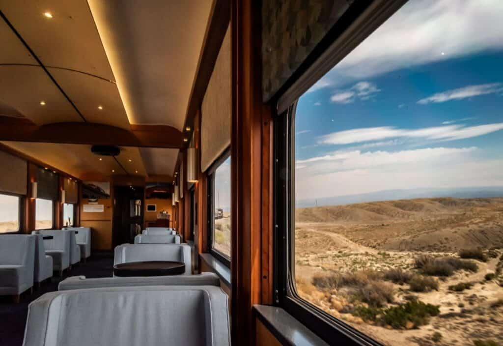 Interior of a train with empty seats and large windows, revealing the Canyon Spirit&mdash;the vast desert landscape and blue sky stretching endlessly outside.