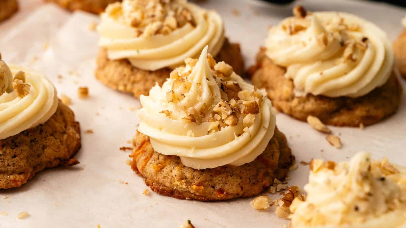 Cookies topped with swirls of cream-colored frosting and sprinkled with chopped nuts, arranged on a sheet of parchment paper.