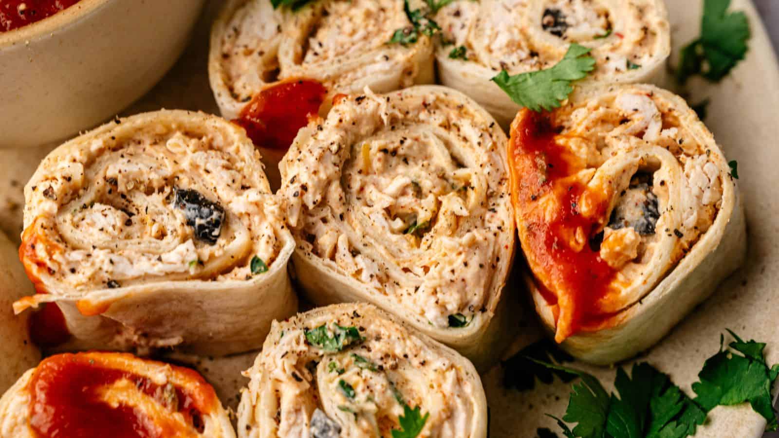 Close-up of several tortilla pinwheel roll-ups filled with shredded chicken, herbs, and sauce, garnished with cilantro.