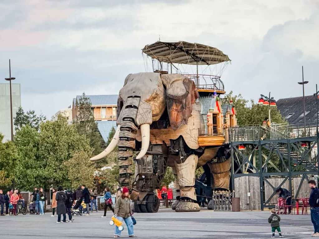 A large mechanical elephant strolls through an open public space in Nantes, with people walking nearby and trees and buildings all around&mdash;an unmissable sight if you have 48 hours in Nantes.