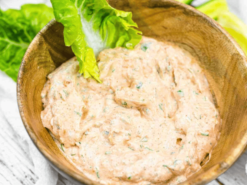 A wooden bowl filled with a creamy, herb-speckled dip, garnished with a fresh green lettuce leaf.