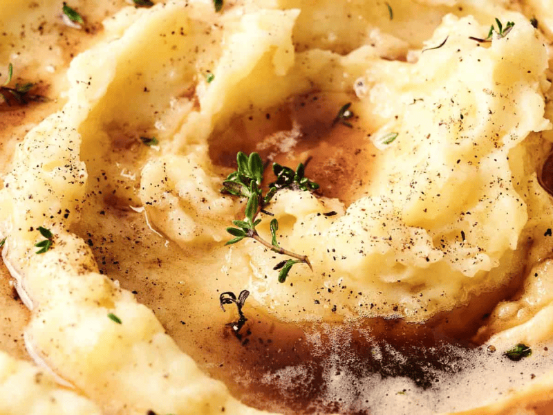 Creamy mashed potatoes topped with gravy and garnished with fresh thyme and cracked black pepper.