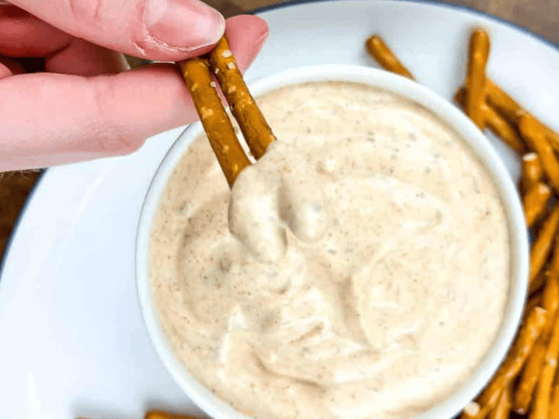 A person dipping a pretzel into a bowl of cajun dip.