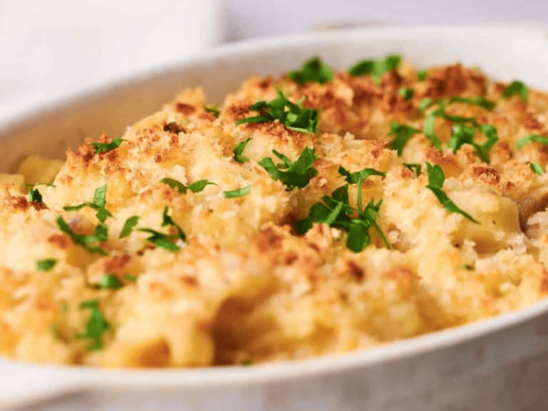 A baking dish filled with golden-brown baked tuna noodle casserole, topped with breadcrumbs and garnished with chopped parsley.