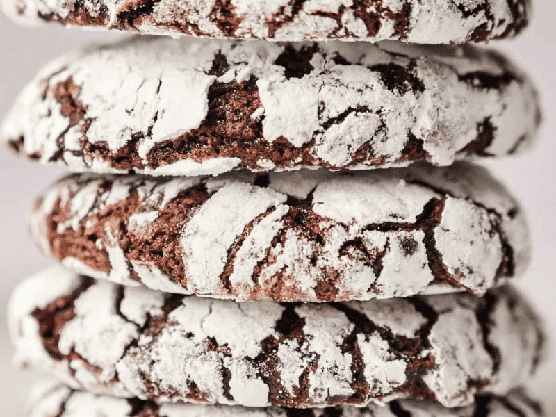 A close-up of a stack of chocolate crinkle cookies coated in powdered sugar.