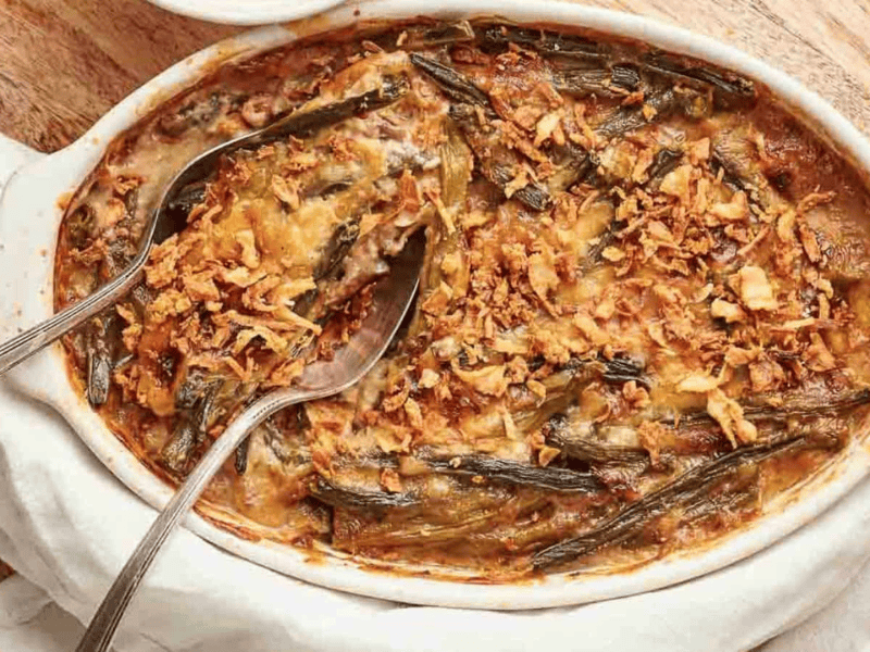 Baked green bean casserole topped with crispy fried onions, served in a white oval dish with a serving spoon.