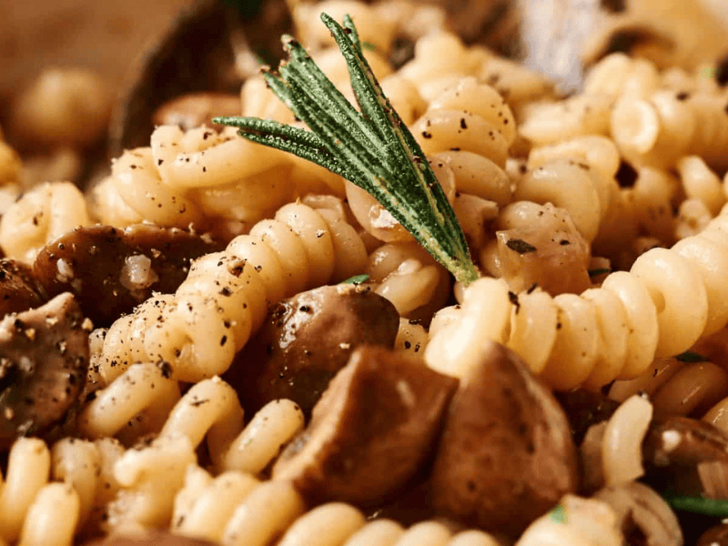 Close-up of fusilli pasta with mushrooms, garnished with rosemary and black pepper.