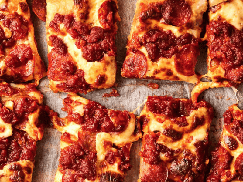 Eight rectangular slices of pepperoni pizza with thick tomato sauce and melted cheese on parchment paper.
