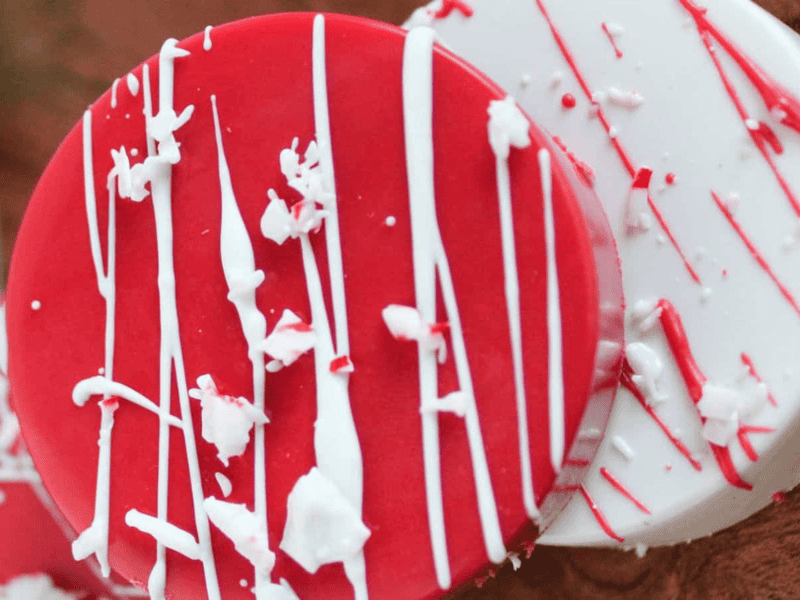 Two round cookies, one red and one white, are decorated with white icing drizzles and white sprinkles, placed on a wooden surface.