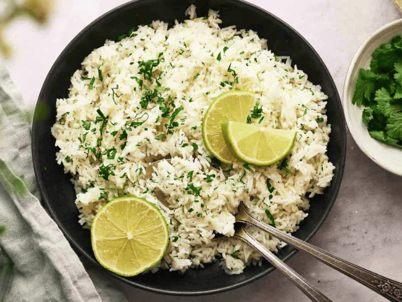 Chipotle rice in a bowl with sliced lime and spoons.