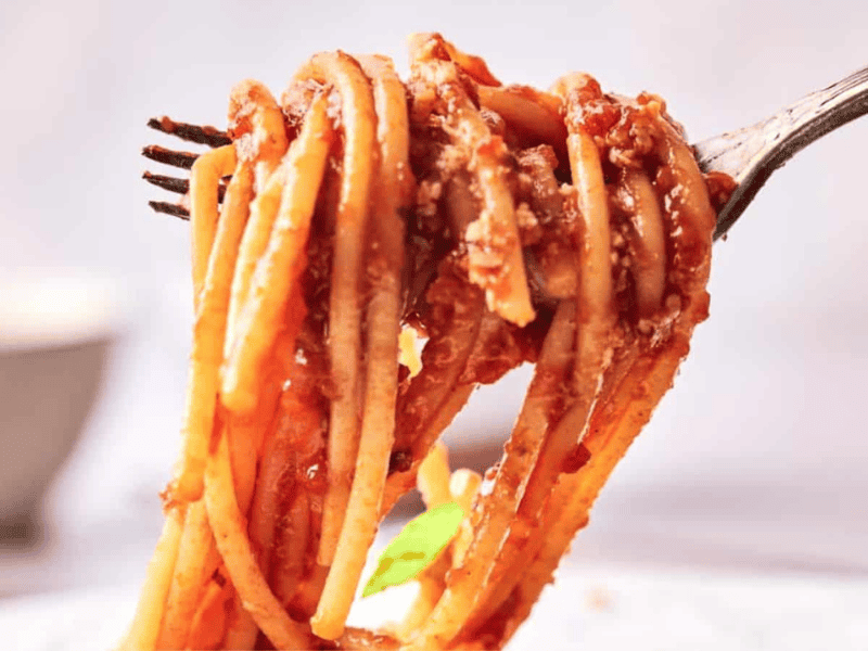 A fork twirls spaghetti noodles coated in red tomato sauce with visible bits of meat or cheese.