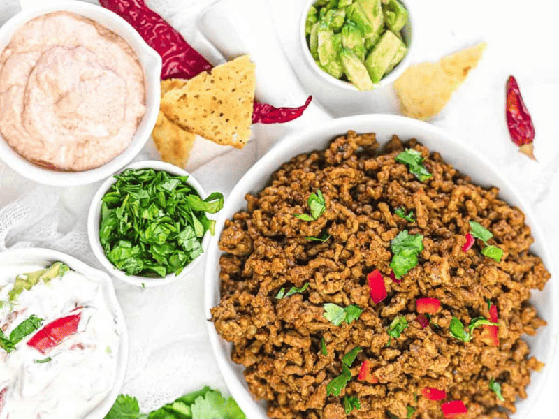Ground Beef Taco Meat inside a white plate with smaller bowls of veggies and sauces.