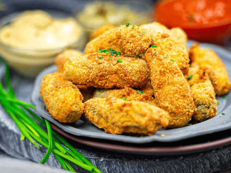 A plate of breaded and fried food items garnished with herbs, with dipping sauces in small bowls in the background.