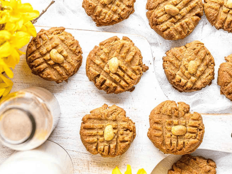 Peanut Butter Keto Cookies layered on a white surface with yellow flowers on the side.