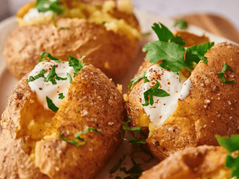 Baked potatoes with crispy skins, topped with sour cream, chopped parsley, and a sprinkle of red pepper flakes.