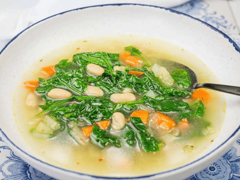A bowl of rice and white bean soup with served with a spoon on a blue and white patterned surface.