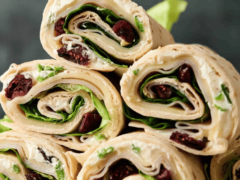 Close-up of stacked tortilla pinwheels filled with spinach, cream cheese, dried cranberries, and lettuce.
