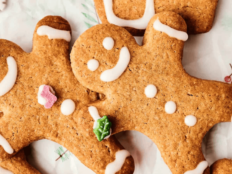 Two gingerbread cookies decorated with white icing and small colorful candy shapes on a light patterned surface.