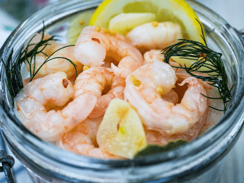 Close-up Southern Style Pickled Shrimp with lemon slices and dill on a jar.
