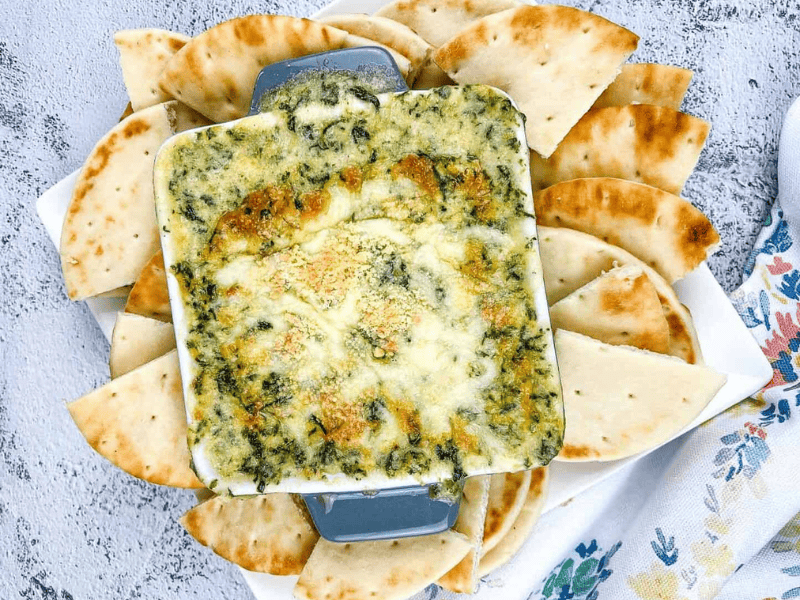Spinach & Brie Dip in a casserole dish surrounded by pita wedges.
