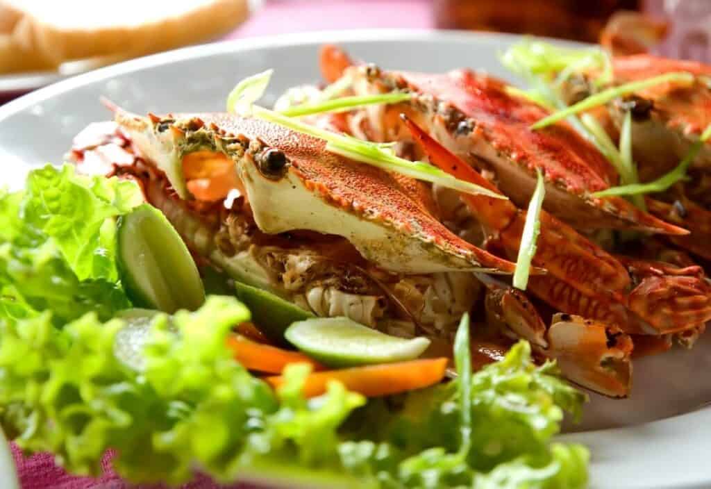 A plate of cooked crabs garnished with sliced green onions, served with fresh lettuce, cucumber, and carrot slices.