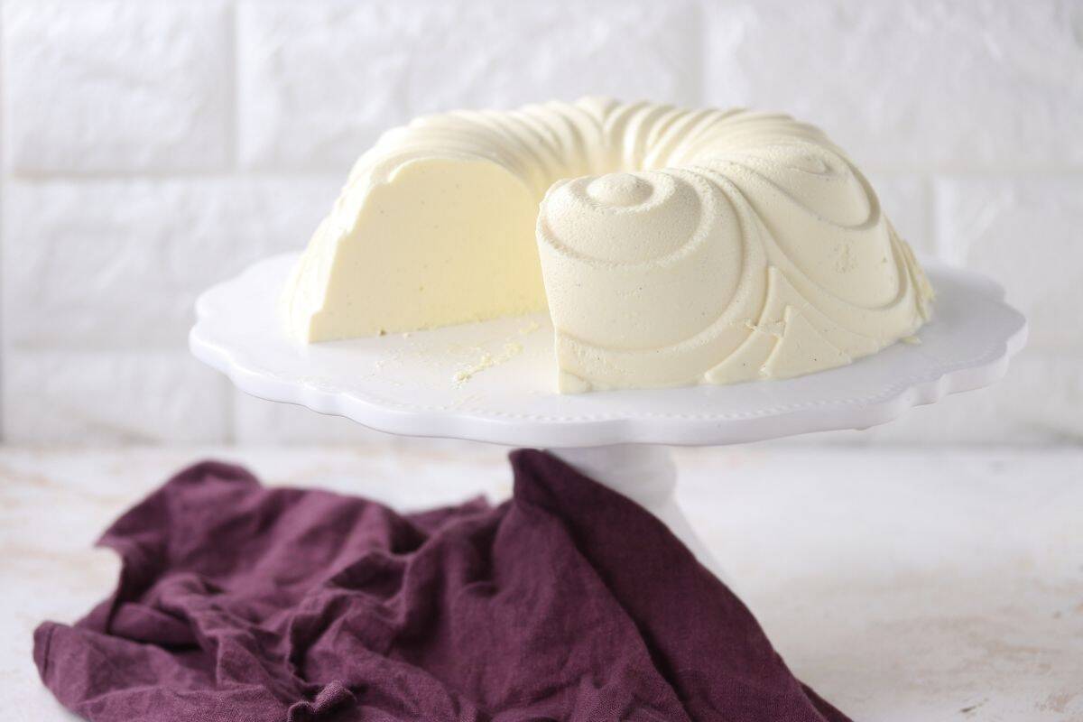 A Vanilla Bavarois dessert with a slice removed is displayed on a white cake stand, with a purple cloth underneath.