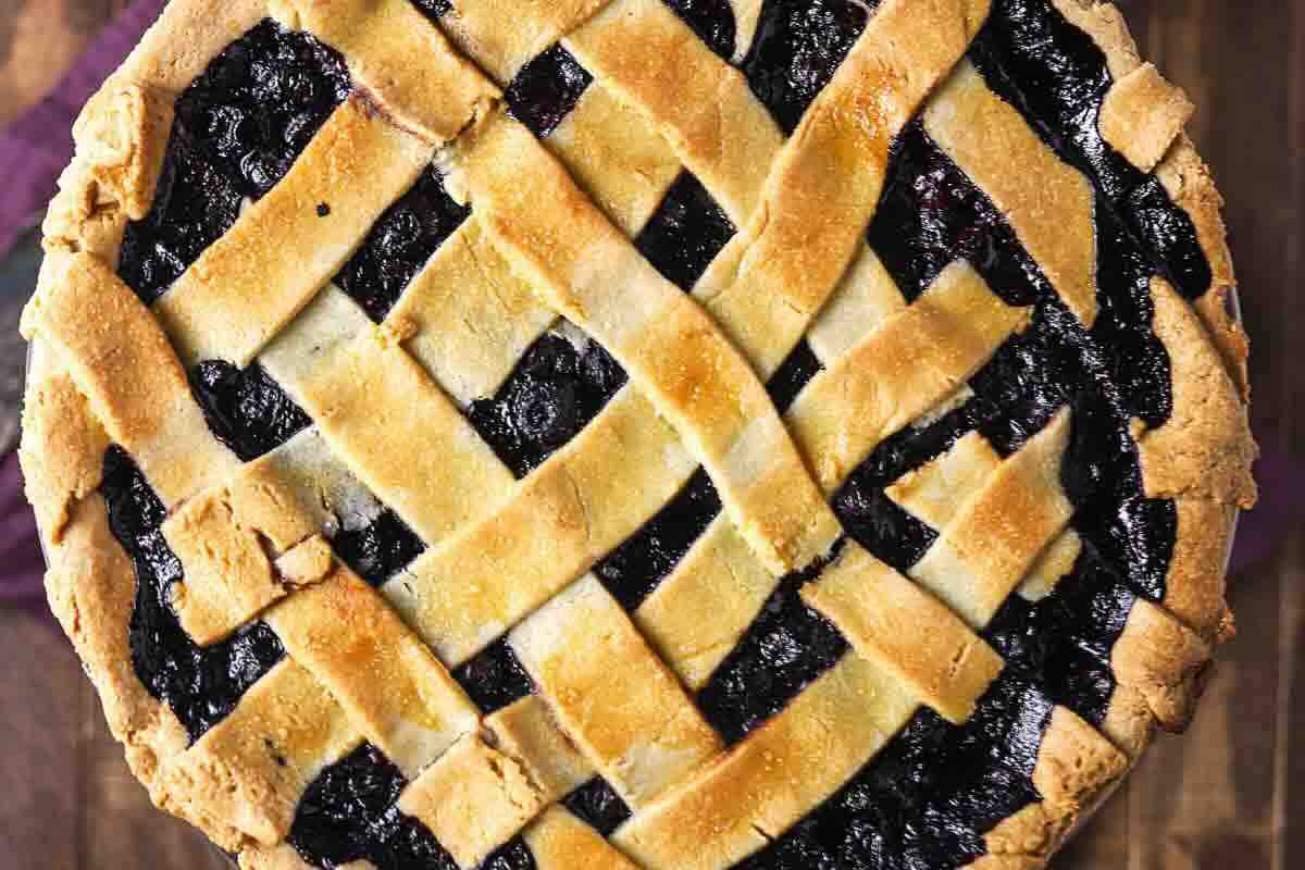 A close-up of a baked pie with a golden-brown lattice crust and dark fruit filling, viewed from above.